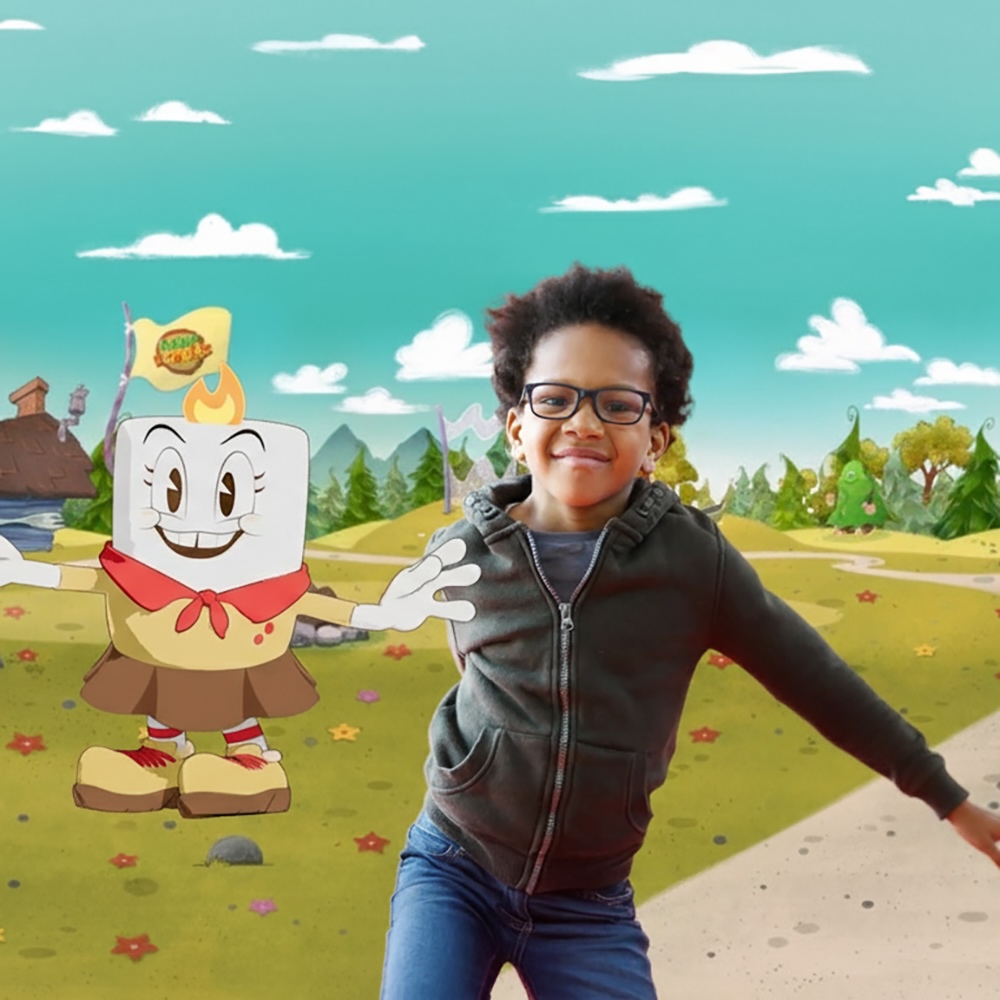 Promotional image for "Camp Bonkers" showing a real child in glasses and a dark hoodie posed alongside an animated marshmallow-headed character with a flame tuft, red bandana, and hiking boots. They stand together in an illustrated outdoor camp setting with green hills, pine trees, a lake with a cabin, and a small flag reading "Camp Bonkers," under a teal sky with clouds.