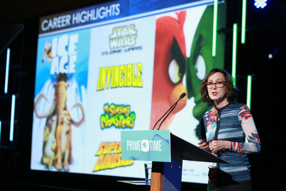 Catherine Winder stands at a podium with "Prime Time" written on it, delivering a presentation / speech at a conference. Behind her, a large screen titled "Career Highlights" displays posters and logos from animated productions including Ice Age, Star Wars: The Clone Wars, Invincible, The Angry Birds Movie, and My Singing Monsters. Vertical LED light bars frame the stage.